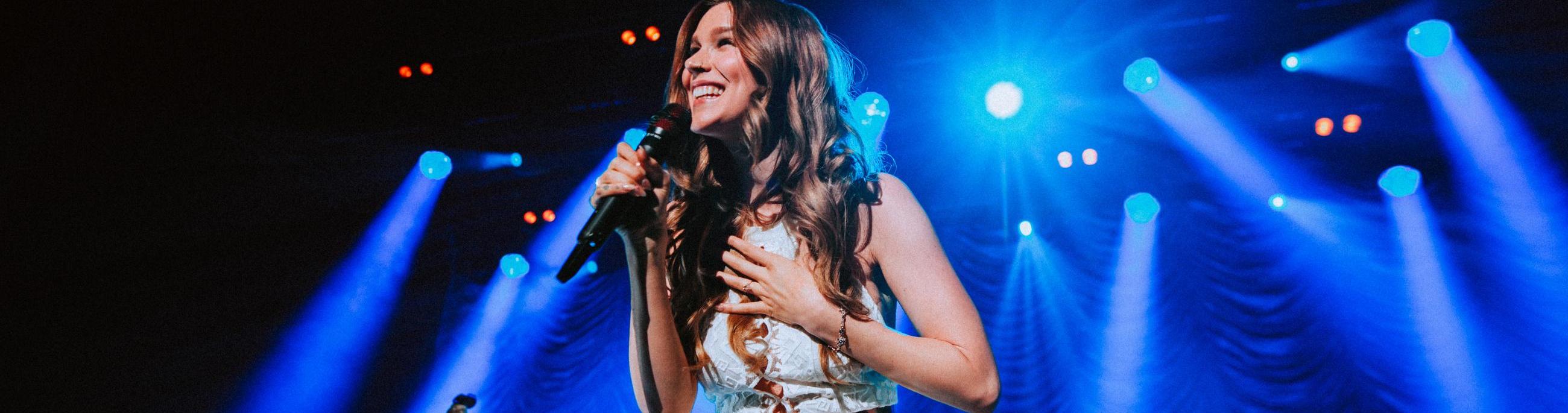 Joss Stone in white dress with blue stage light beaming behind her
