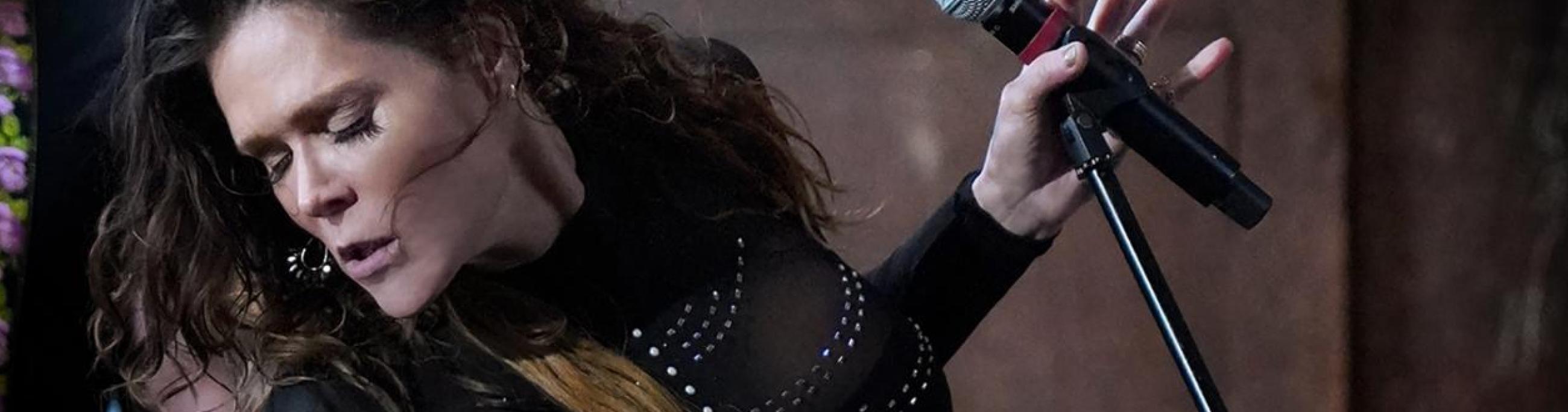 woman standing at a microphone wearing all black and looking away