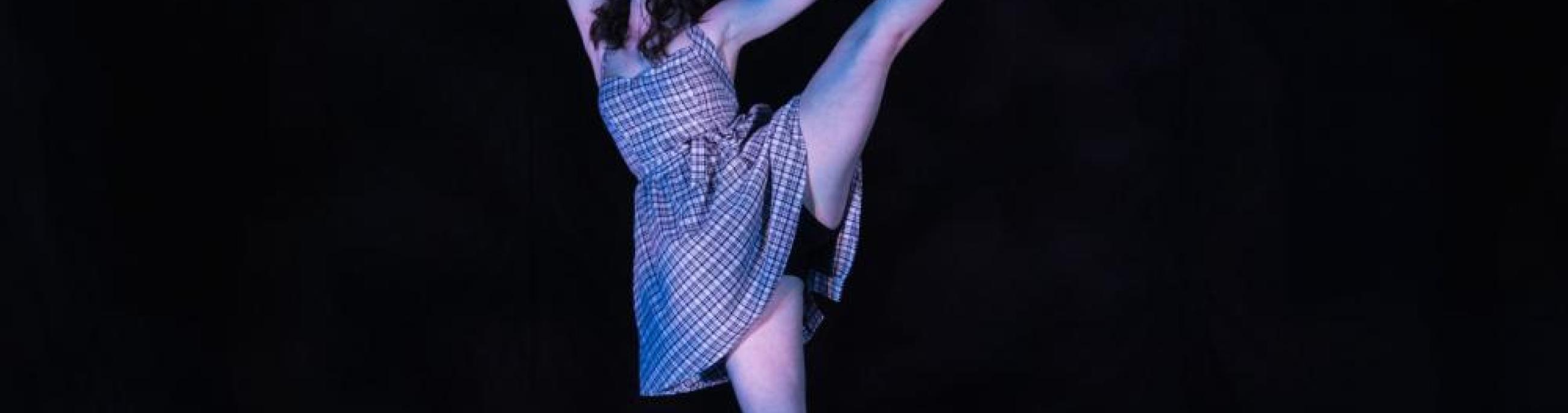 A dancer in a white dress gracefully extends one leg skyward.