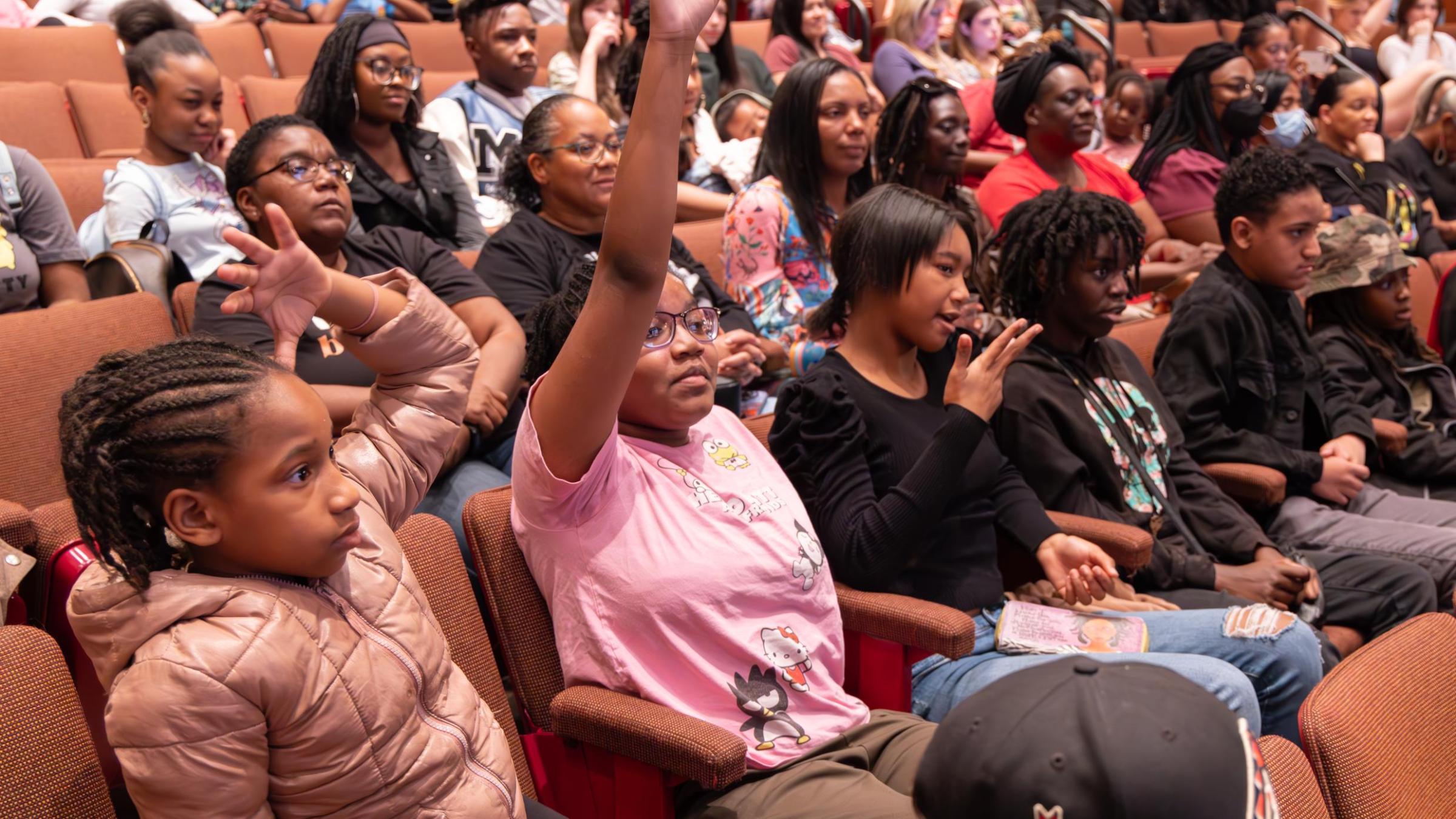students in theatre seats with one raising their hand
