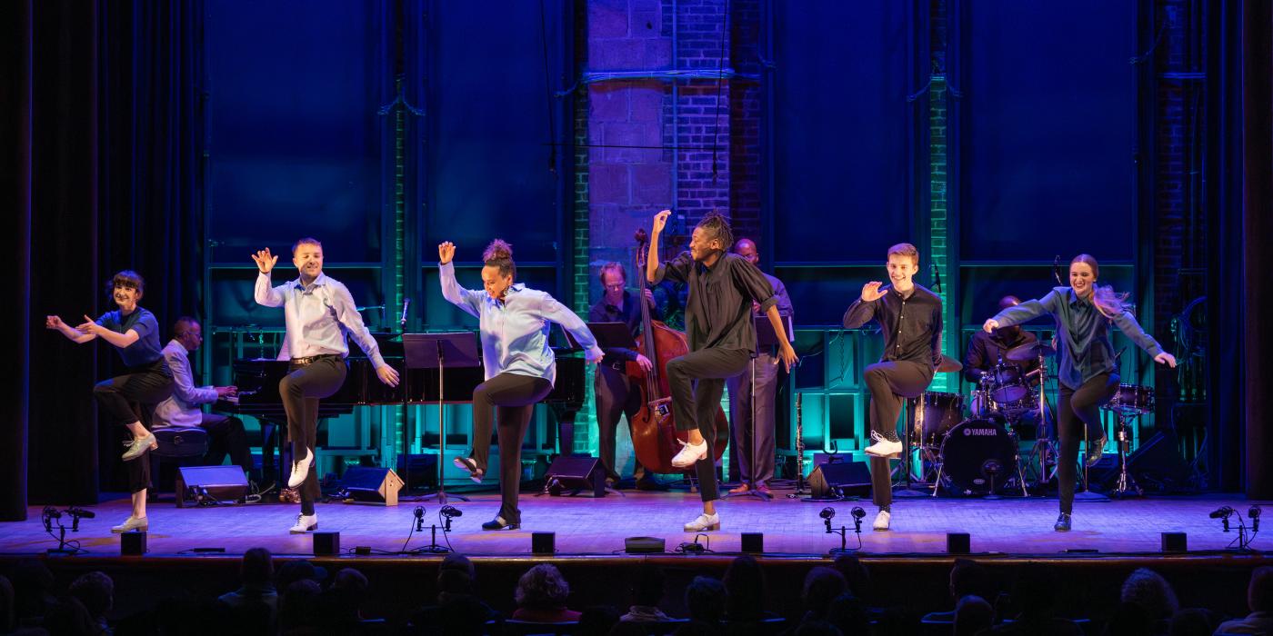 six dancers on stage smiling with right arms up and left knees raised up