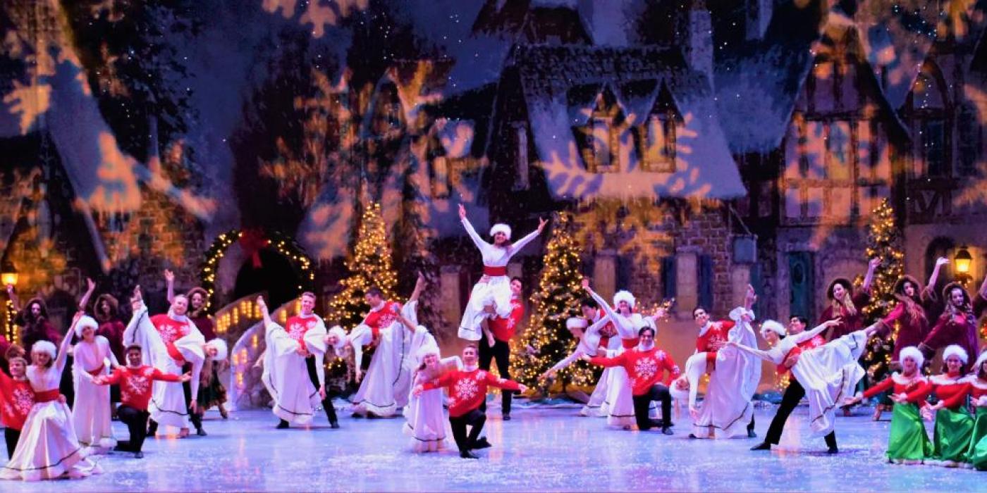 Group of dances on stage dressed in white dresses, red sweaters with snowflake shaped lighting