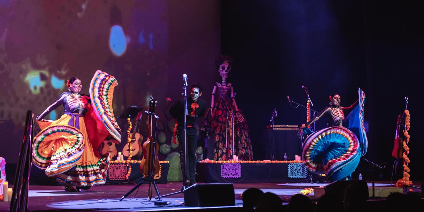 3 performers on stage twirling traditional Mexican dresses and man dressed in black