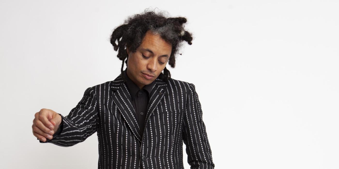 Black man with dreadlocks standing in a black suit with white pinstripes