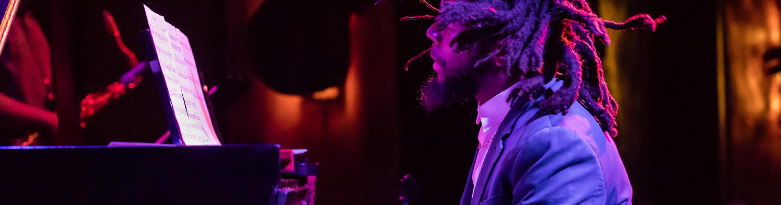 man with dreads playing the piano. the shot is taken from the left of him, making him in profile