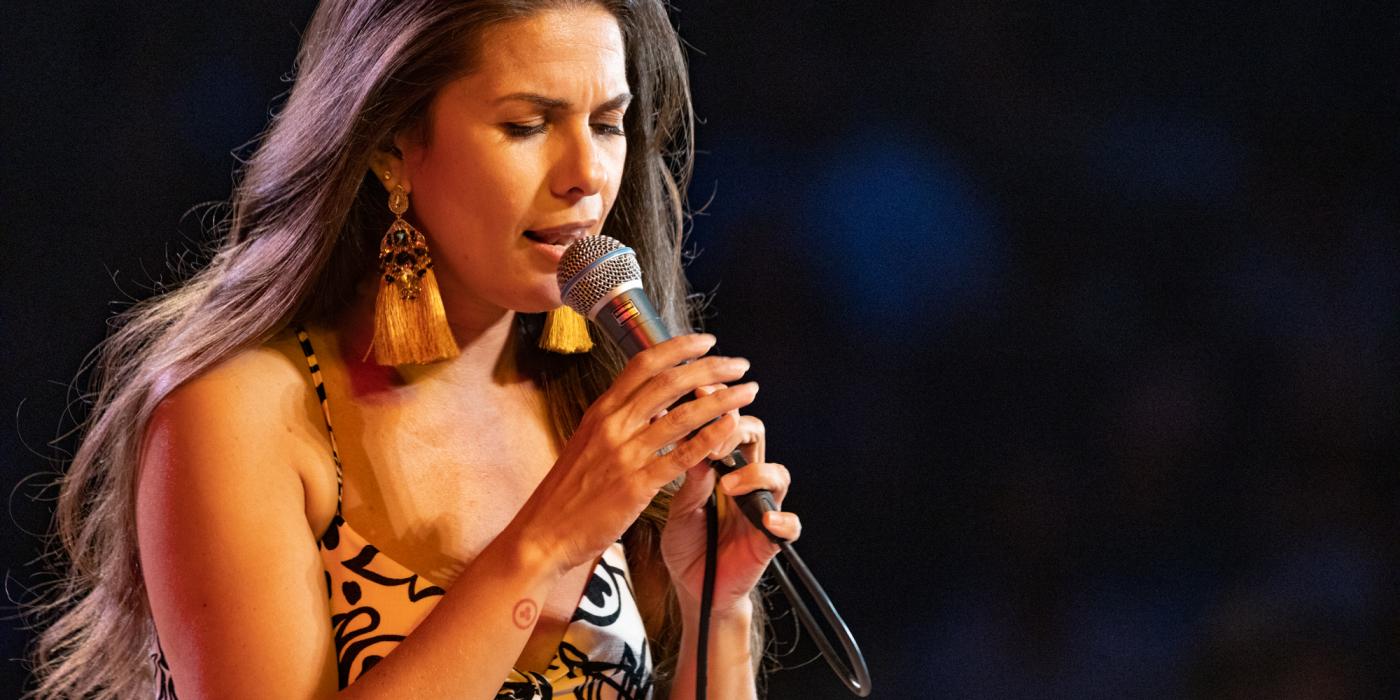 Brazilian vocalist Caro Pierotto singing on dark stage with mic in her hands