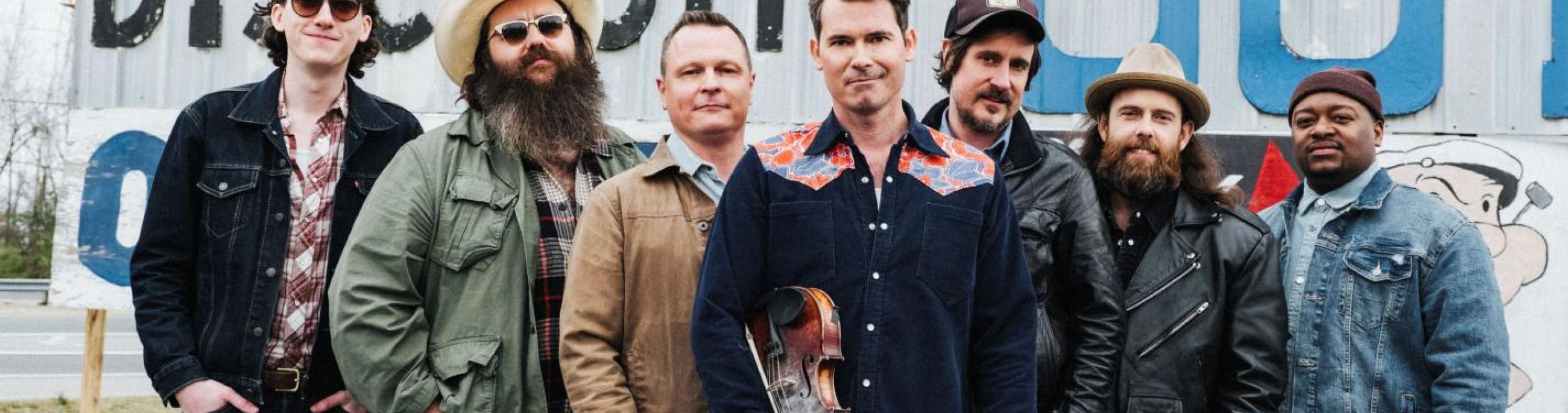 seven men standing in jeans and shirts and cowboy hats looking at the camera