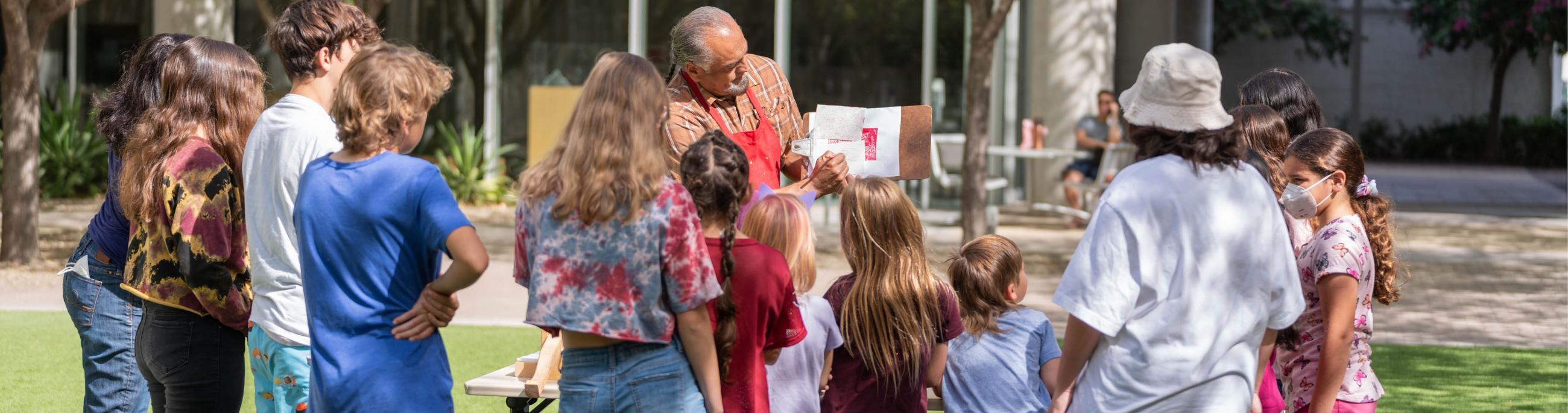 Youth watch a teaching artist explains the printing process