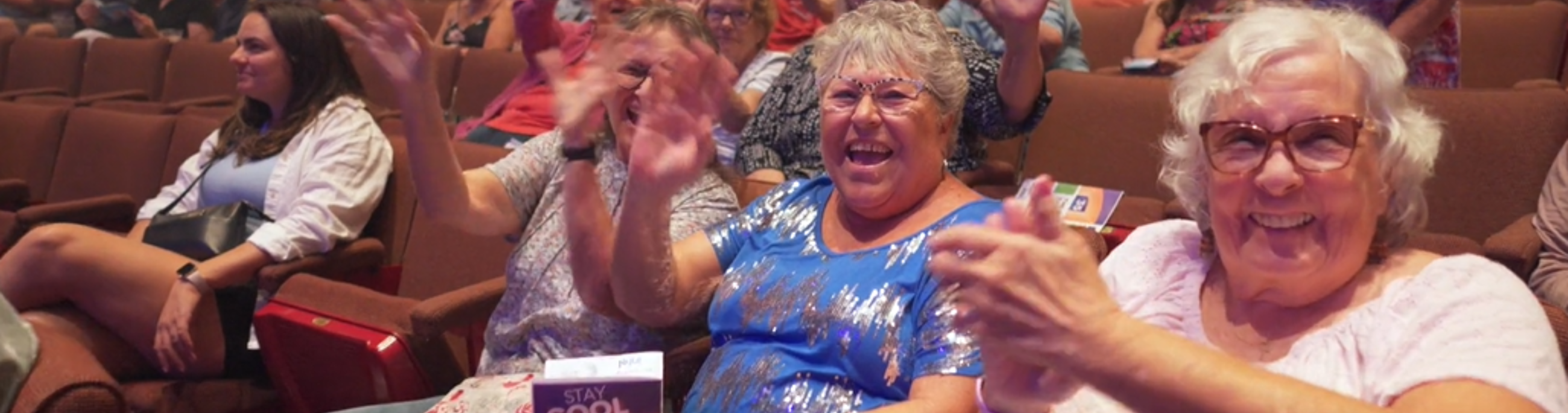 patrons smiling and waving from theatre seats